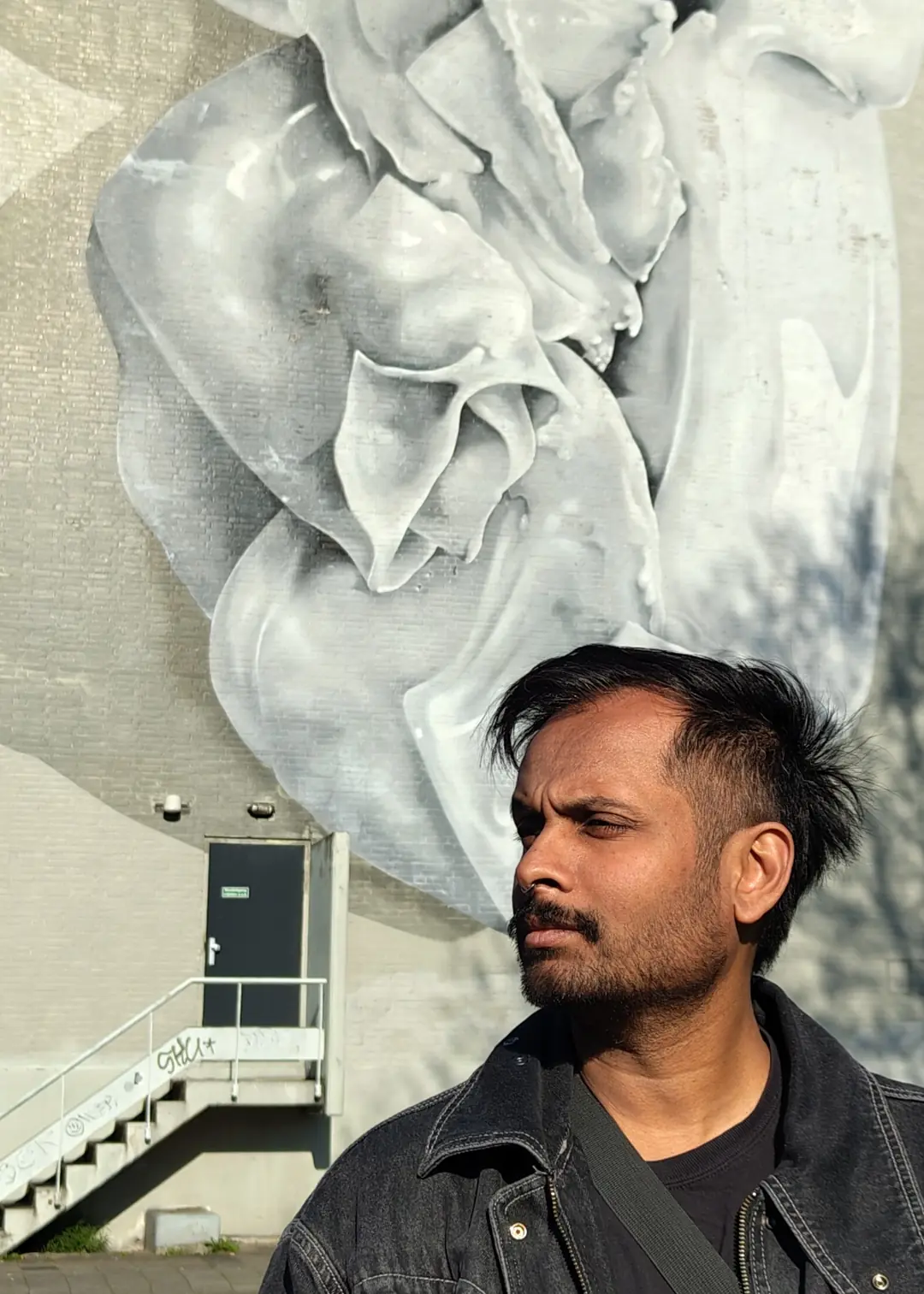 Akshay Gite in front of a large mural of a white folded form, Berlin, 2026